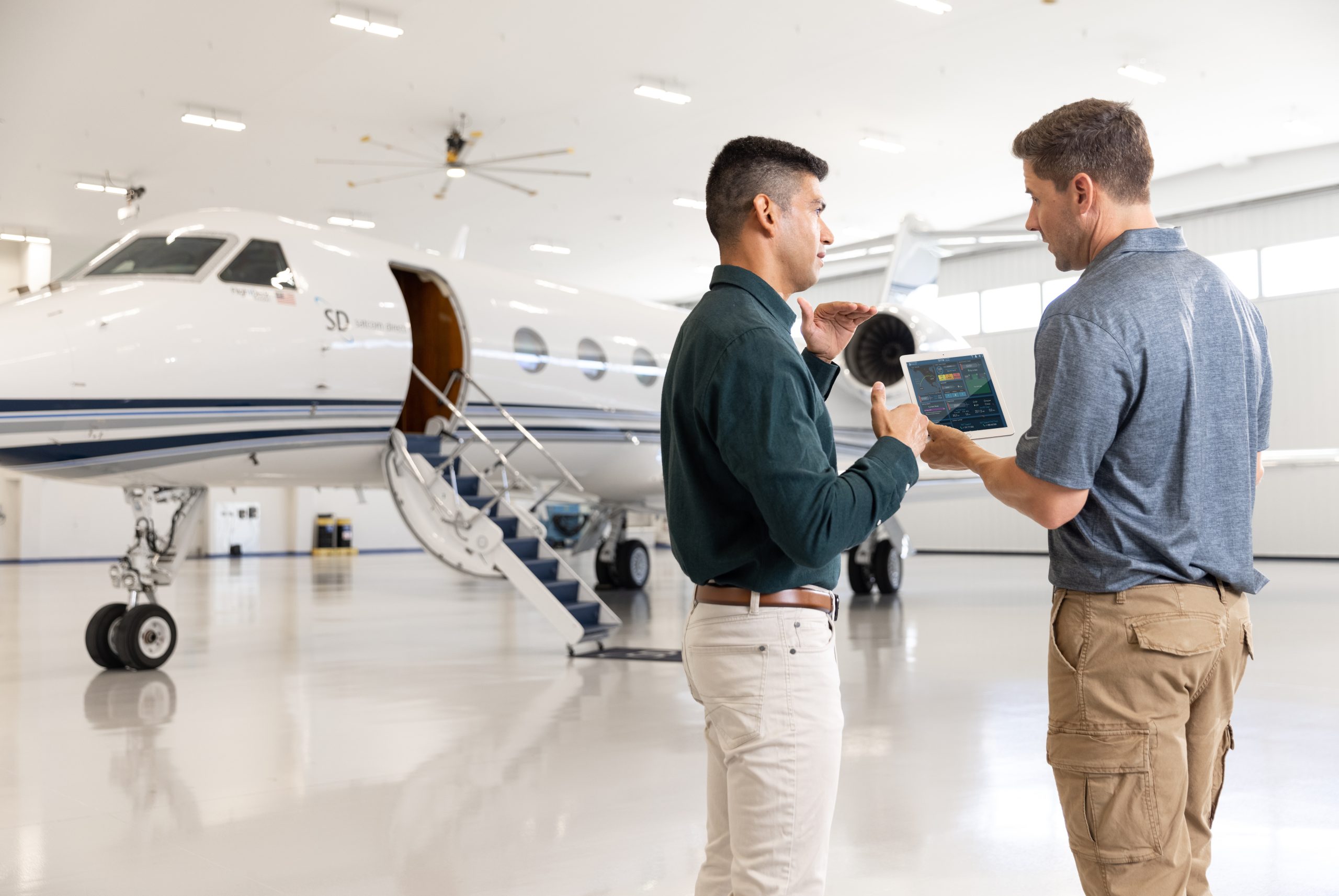 two men in airplane hanger talking over iPad